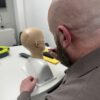 Bald man removing ear wax from mannequin whilst being trained