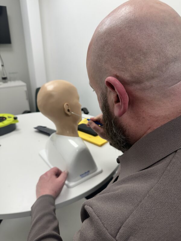 Bald man removing ear wax from mannequin whilst being trained
